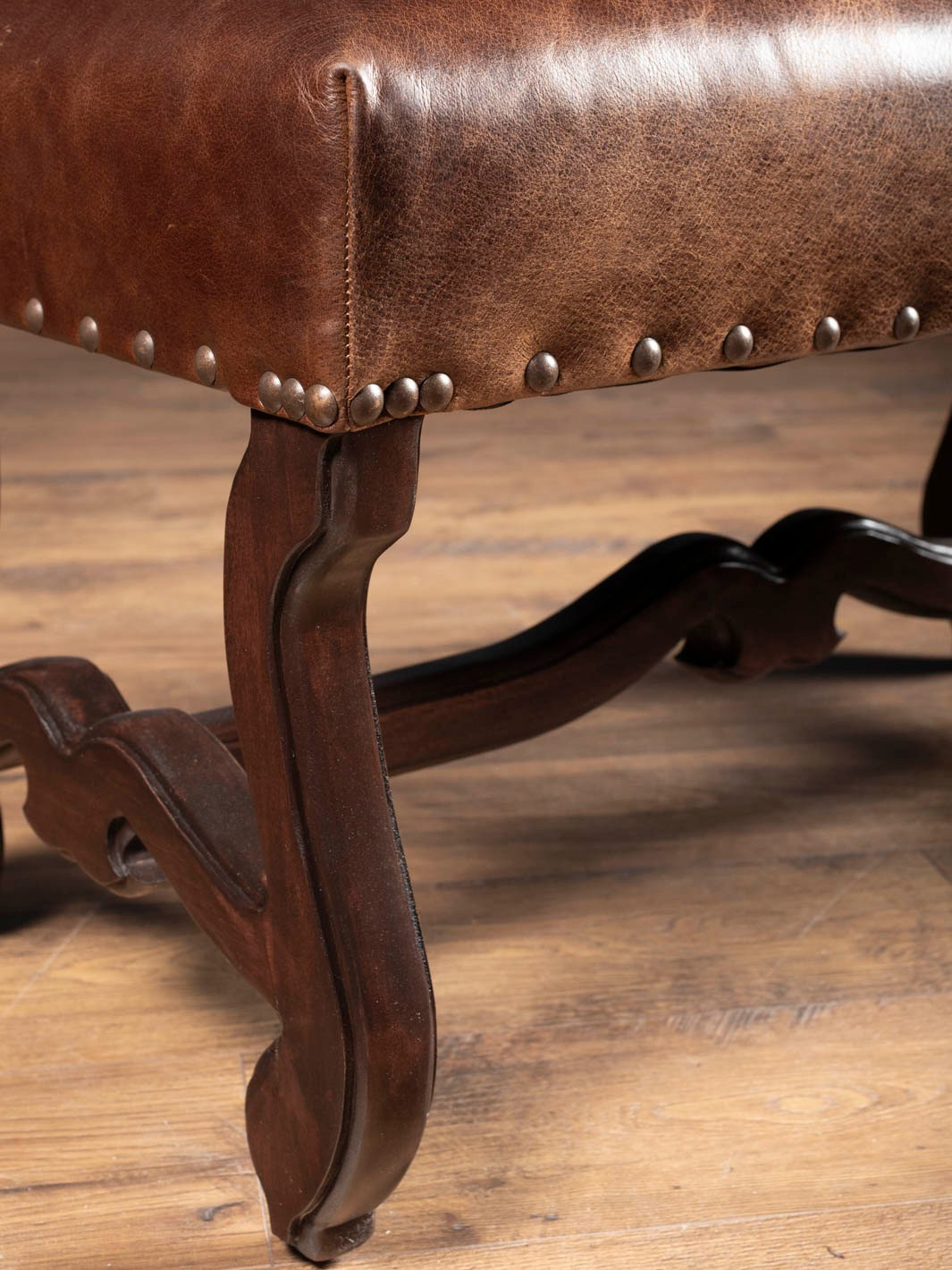 Close up view of the Vaquero Leather Bench showing the brown buffalo leather texture, antiqued metal nailhead trim, and  curved Spanish Revival cabriole leg details.