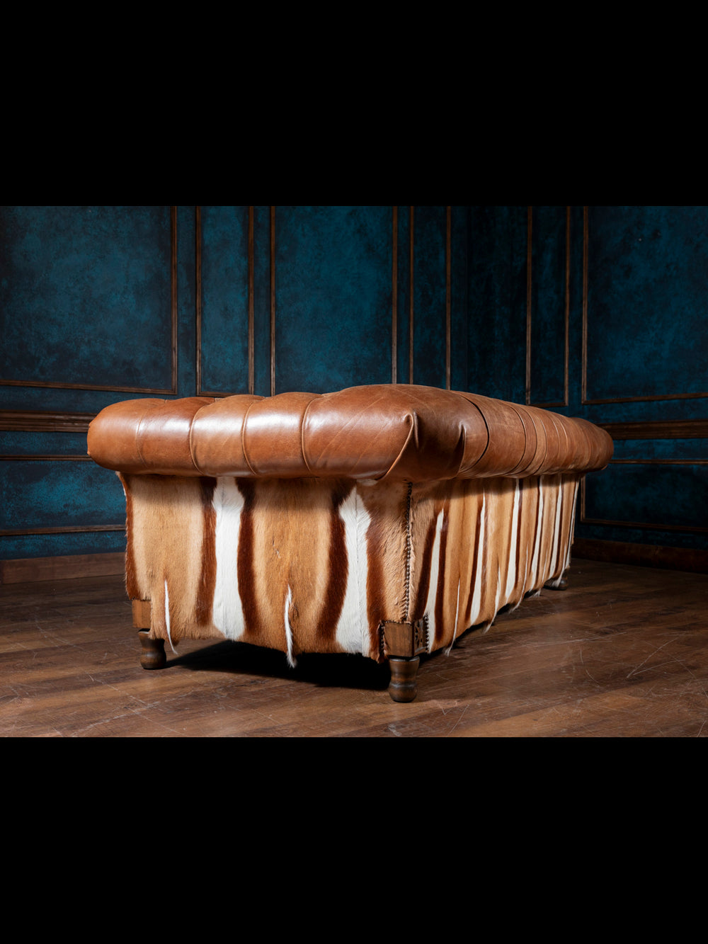 Brown leather ottoman with cowhide pattern against a dark blue wall.