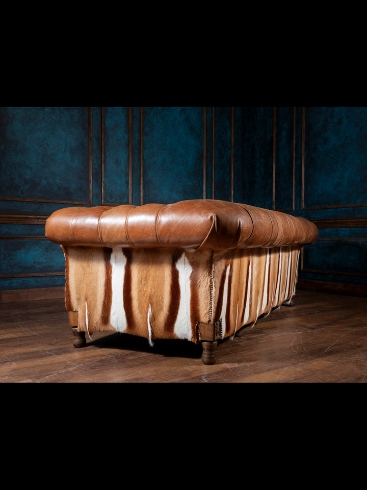 Brown leather ottoman with cowhide pattern against a dark blue wall.