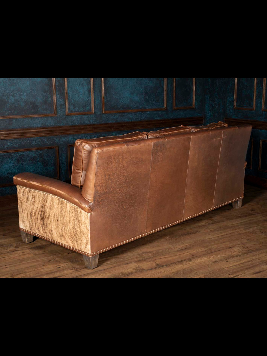 Rear view of Heritage Whipstitch sofa with brown leather back panels, a natural cowhide side and nailhead trim.