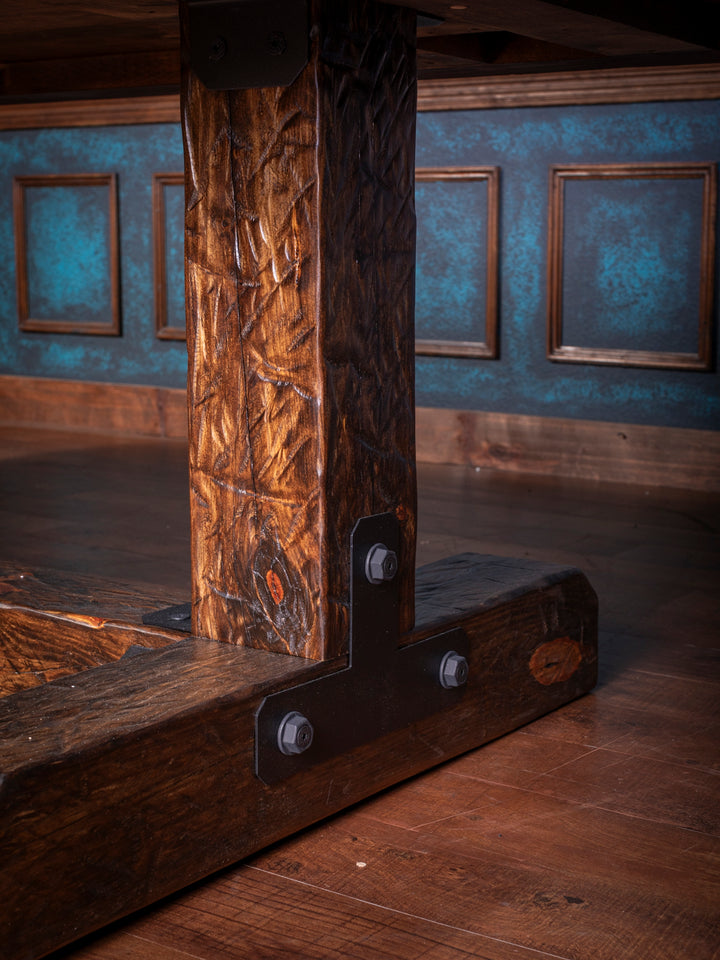 Knotty Alder Rustic Dining Table with carved trestle leg and black steel bracket base detail in a close up view.