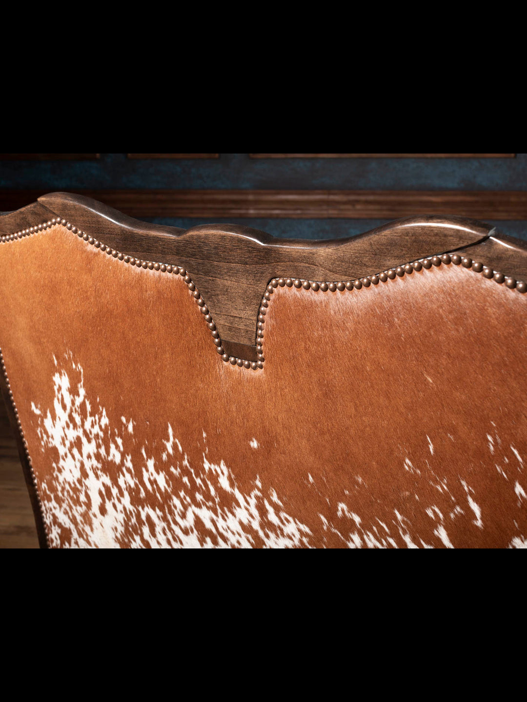 Close-up of the Longhorn Leather Bench featuring a genuine speckled red hair-on-hide back, hand-carved hardwood crest, and decorative brass nailhead trim.
