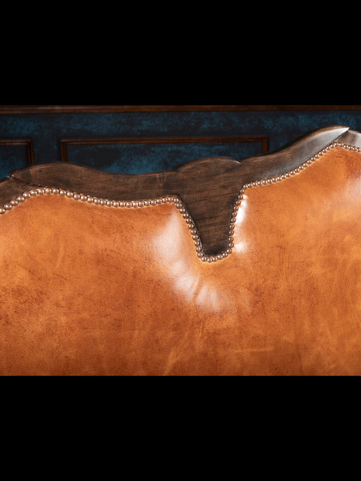 Close-up of the Longhorn Leather Bench featuring a hand-carved longhorn crest, full-grain buffalo leather upholstery, and decorative brass nailhead trim.