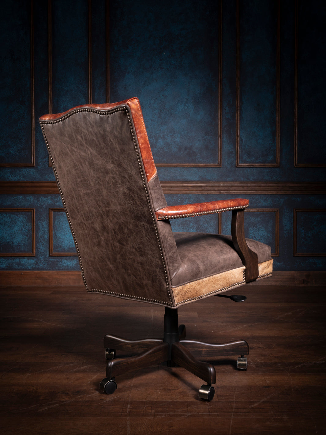 Rear angle of a longhorn leather desk chair showcasing the smooth leather back with decorative nailhead trim and a robust swivel base for easy mobility.