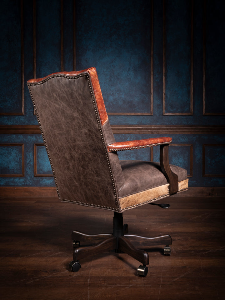 Rear angle of a longhorn leather desk chair showcasing the smooth leather back with decorative nailhead trim and a robust swivel base for easy mobility.