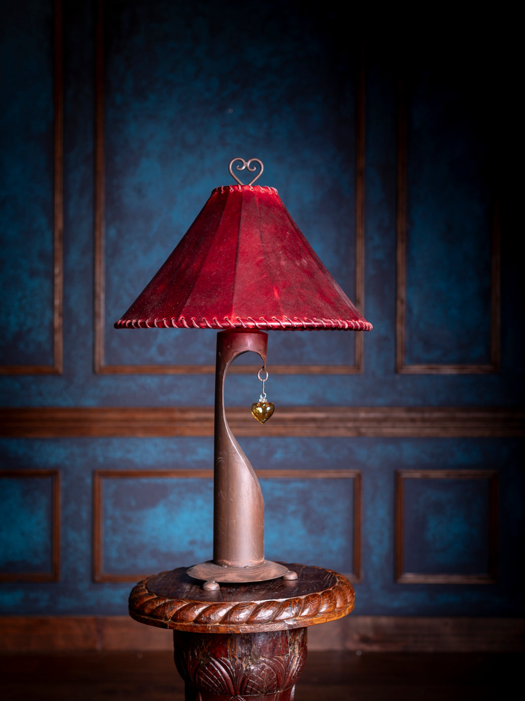 Decorative lamp with a red shade against a dark blue wall.
