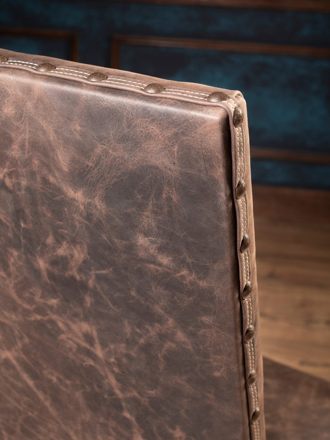 Mustang Leather Dining Chair with brown leather upholstery and brass nailhead detailing along the trim in a close up view.