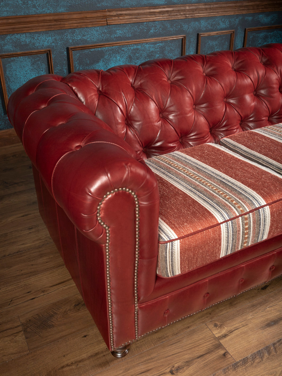 High angle overview of a hand tufted oxblood burgundy leather ranch sofa with three removable Southwestern style striped fabric cushions.