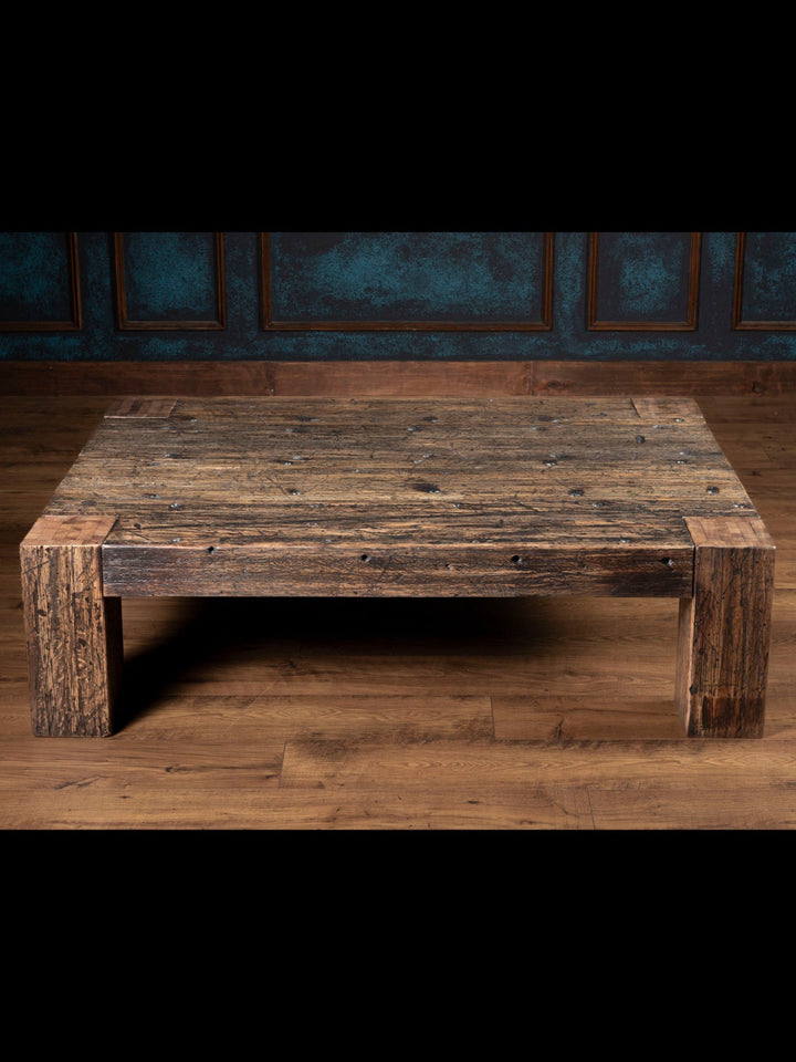 Reclaimed Oak Plank Coffee Table with distressed wood and thick plank legs in a rustic room. 