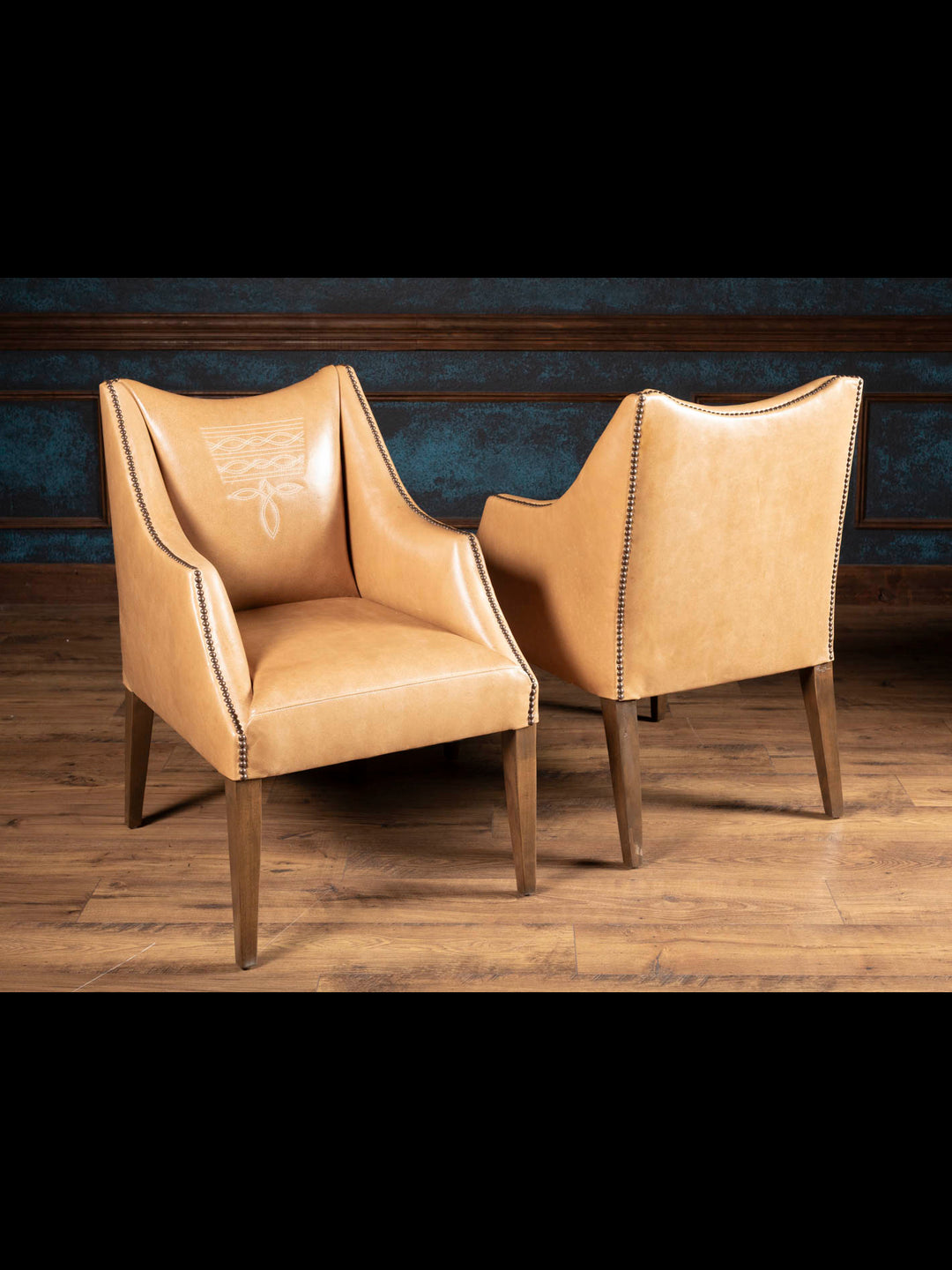 Pair of Ridgecut Western leather dining arm chairs handcrafted with premium buffalo leather, boot stitch detailing, and sculptural dropped-arm silhouettes.