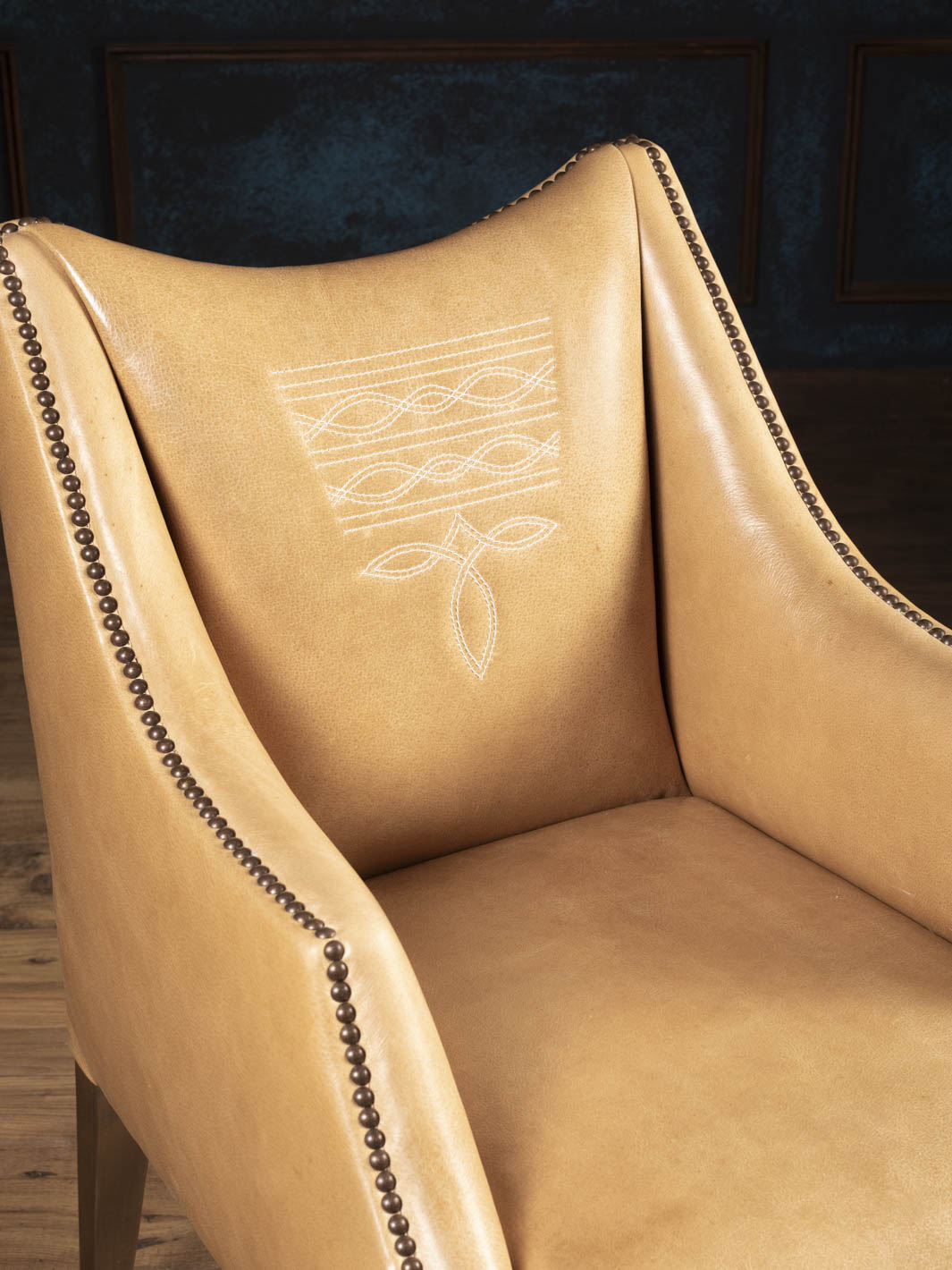 Close-up of the Ridgecut Western leather dining arm chair showcasing premium buffalo leather, signature boot stitch detailing, and decorative brass nailhead trim.