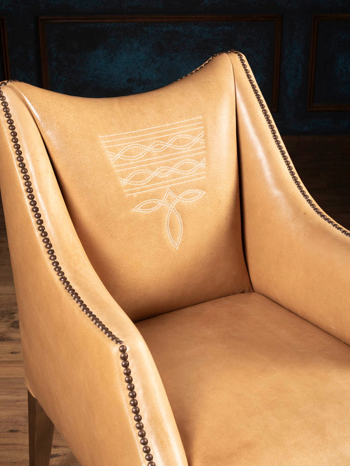 Close-up of the Ridgecut Western leather dining arm chair showcasing premium buffalo leather, signature boot stitch detailing, and decorative brass nailhead trim.