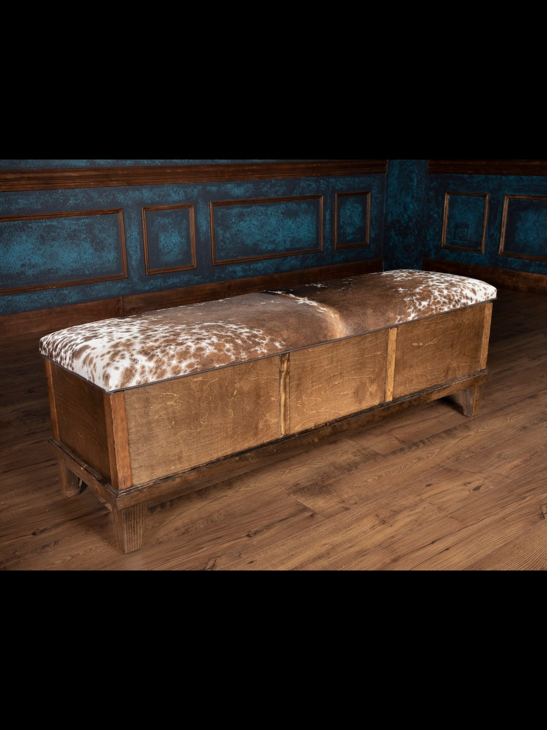 Wooden bench with cowhide cushion in a room with blue paneled walls.
