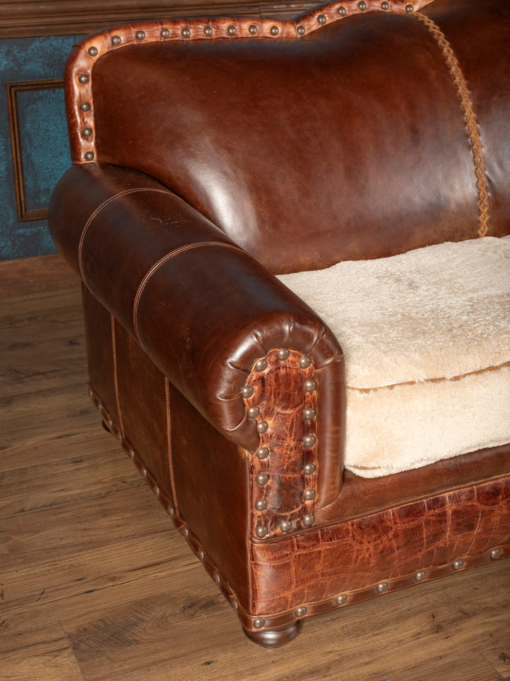 Left-side profile of a Western rolled arm leather sofa featuring an authentic plush cream shearling hide seat cushion.