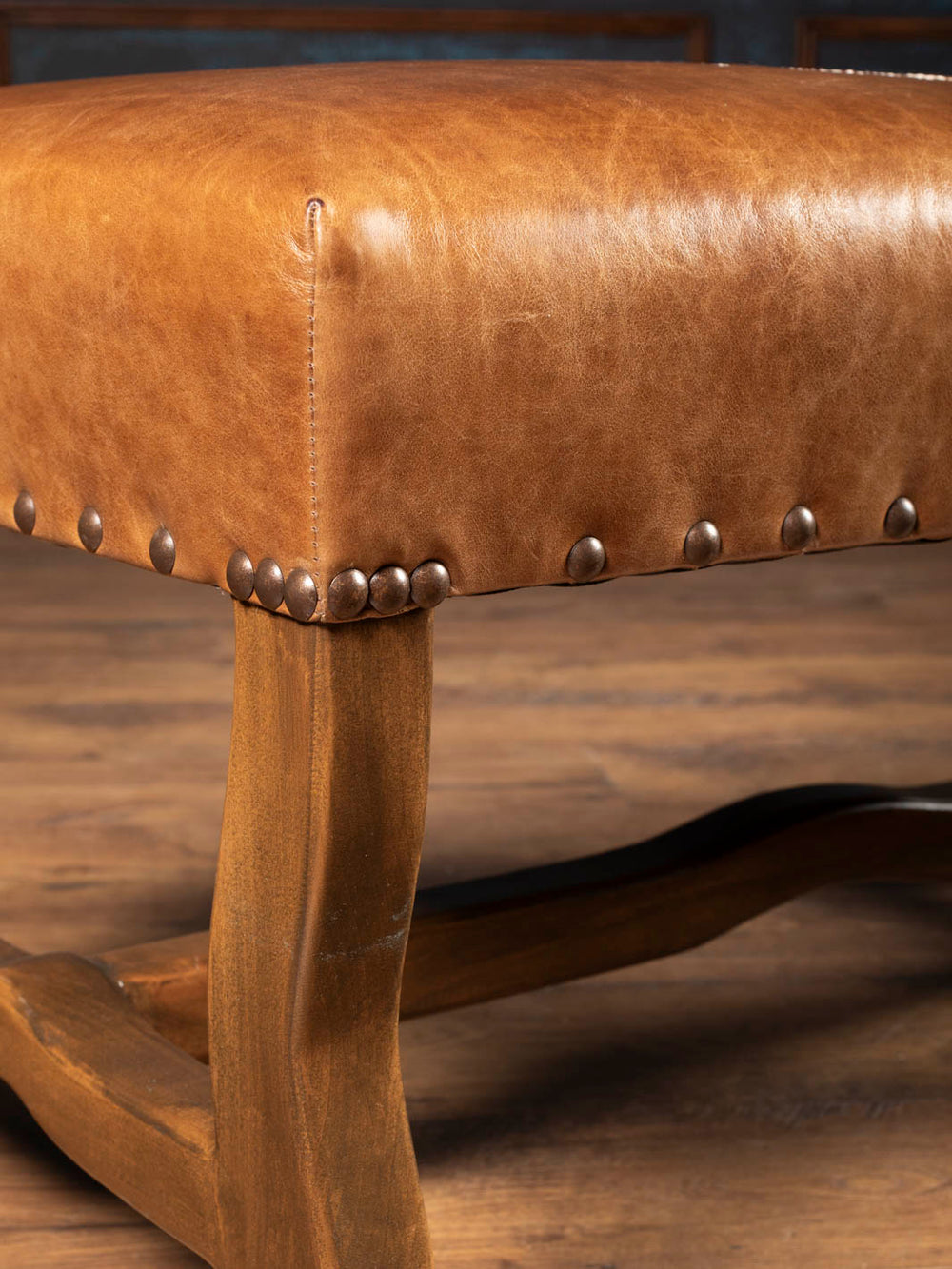 Close-up of Saddle Reserve Santa Fe Bench with saddle brown aniline leather, brass nailheads, and sculpted wood frame.