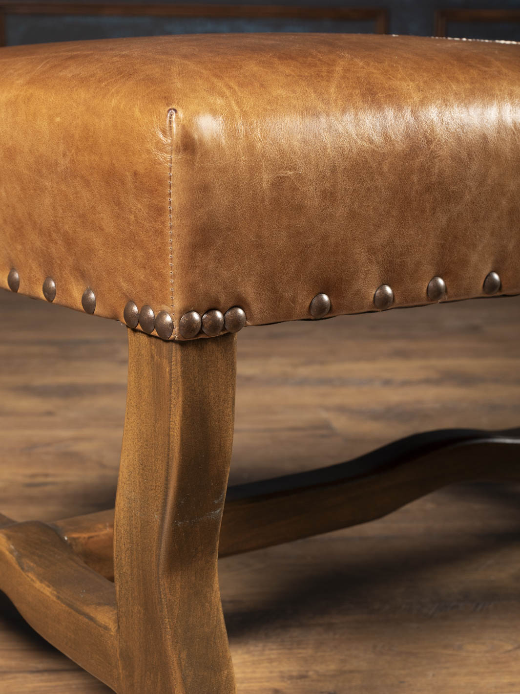 Close-up of Saddle Reserve Santa Fe Bench with saddle brown aniline leather, brass nailheads, and sculpted wood frame.