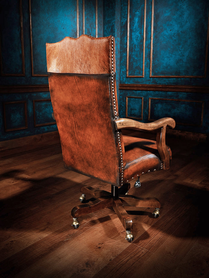 Sanderson Western Leather Desk Chair in burnished Puglia brown leather with brass nailhead trim and sculpted wood arm in a rustic interior space. 