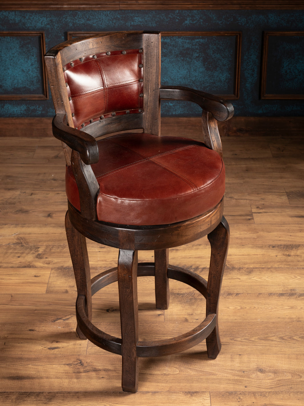 Wooden bar stool with brownish red leather seat and backrest on a wooden floor.