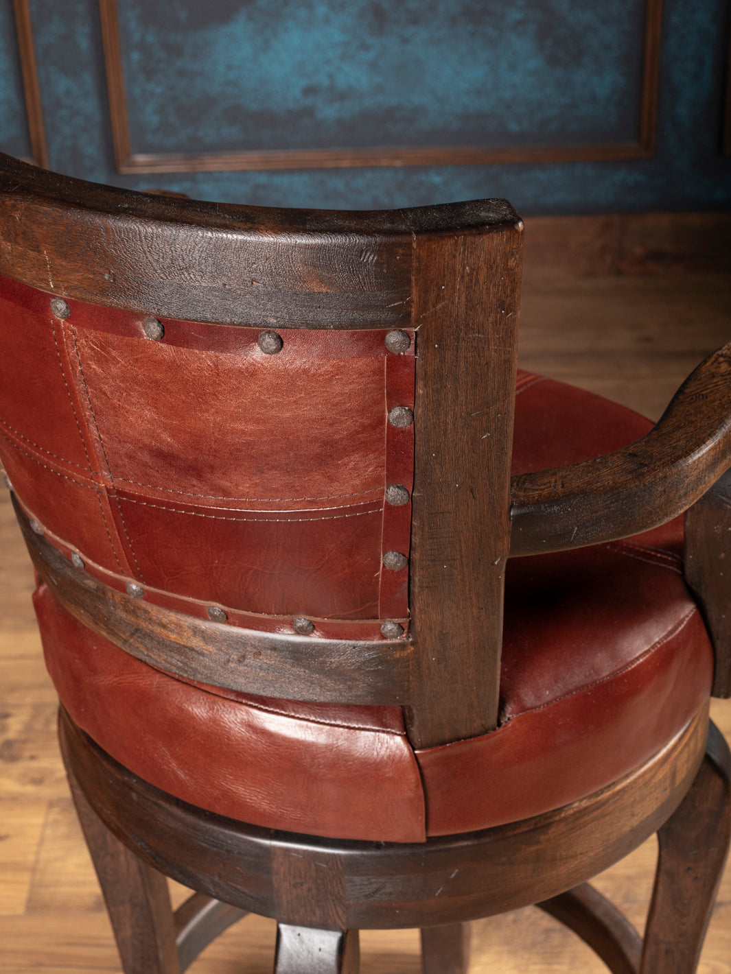Vintage wooden bar stool with leather seat and backrest in a room setting.