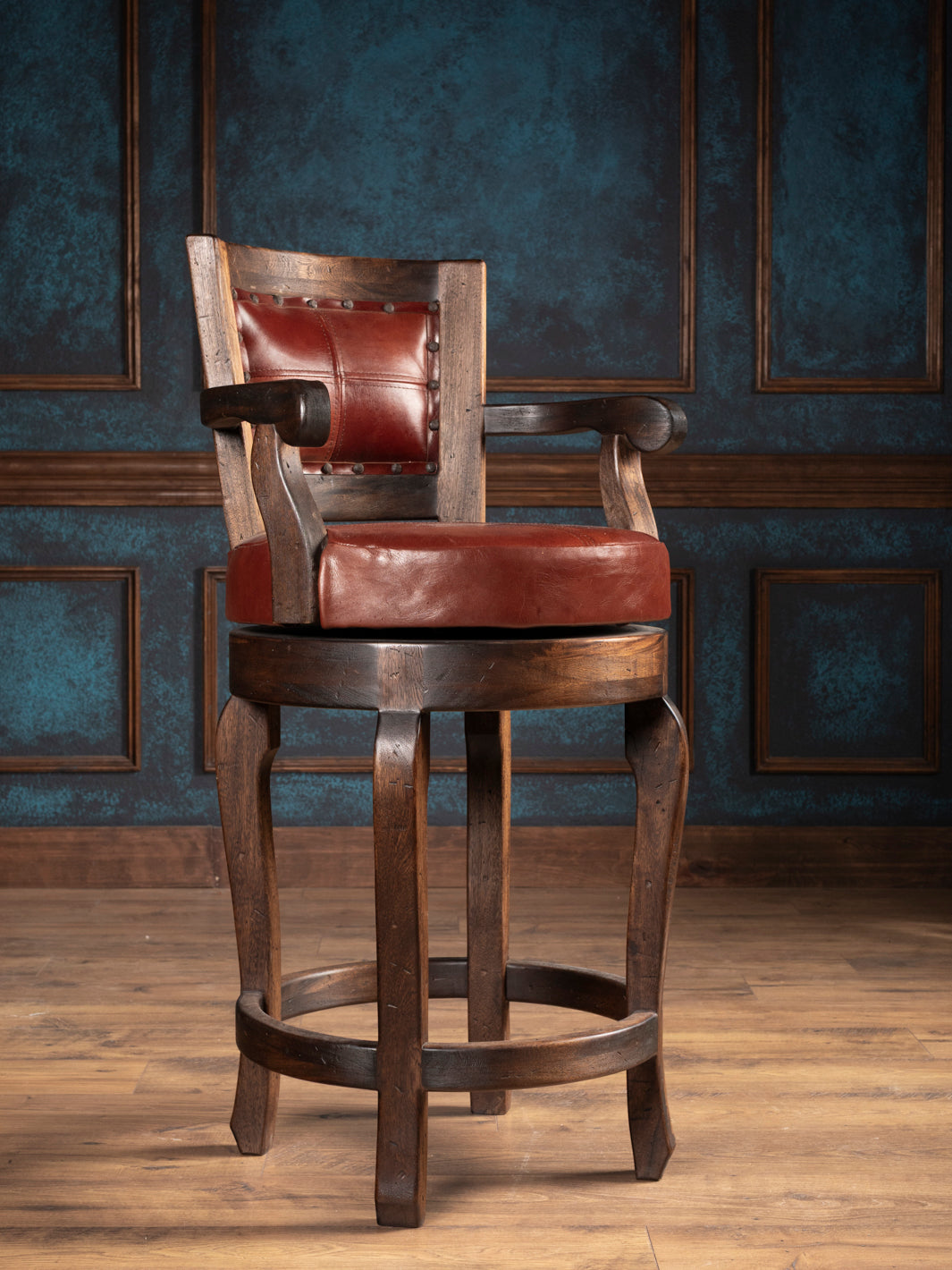 Wooden bar stool with red leather seat and backrest against a dark blue wall.