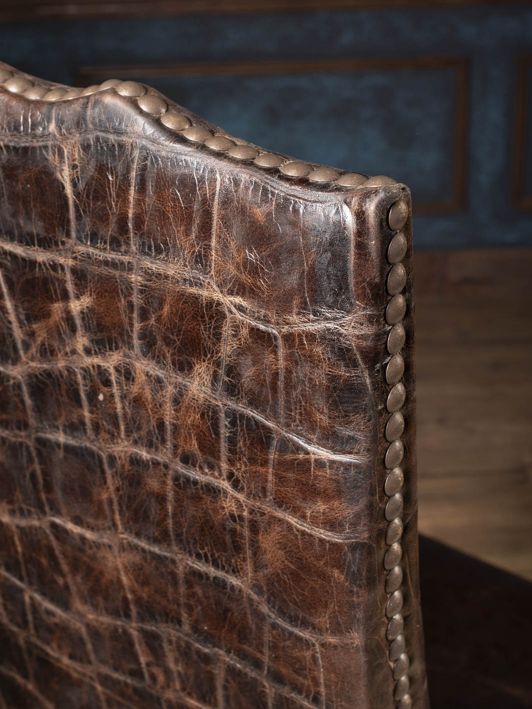 Close up view of the scalloped top crest on a jumbo crocodile embossed leather chair back highlighted by individually hand driven antique brass nailheads.
