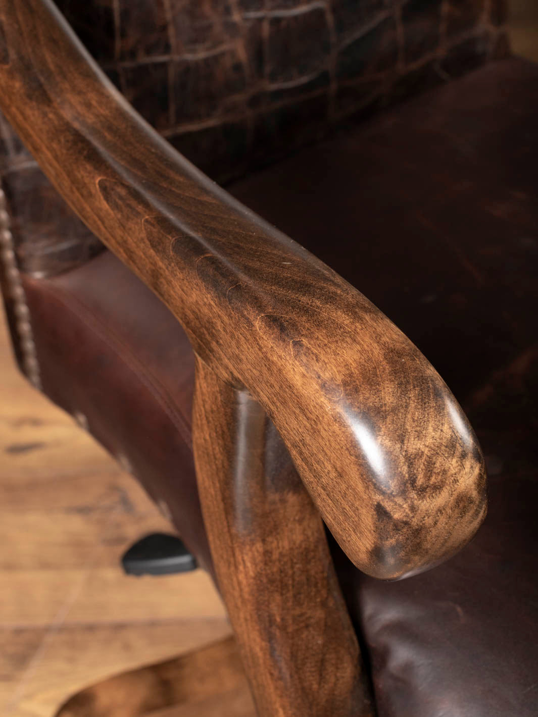 Close up view of a beautifully sculpted solid hardwood armrest showing natural wood grain on a Western leather desk chair.