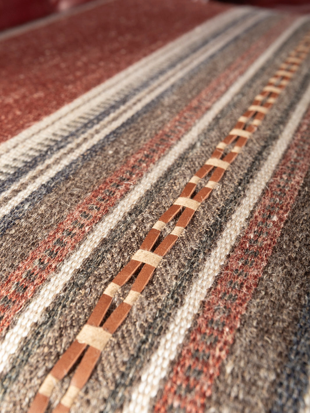Macro detail view of the custom Southwestern patterned fabric sofa cushion highlighting the textured weave and woven leather lace accent strip.