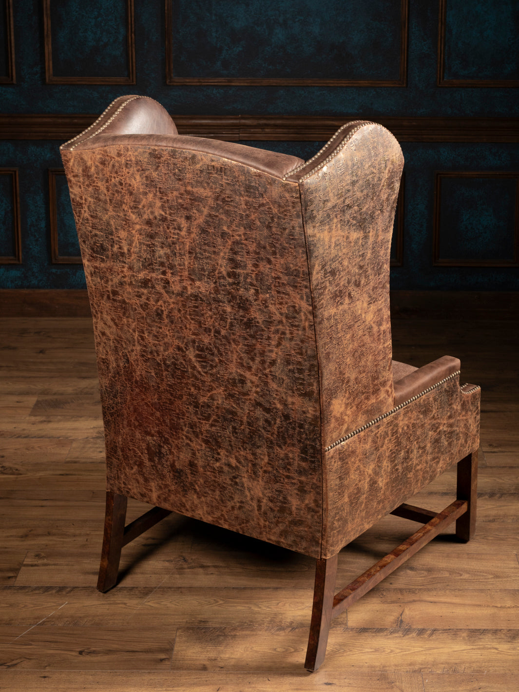 Rear view of the Stockman Western leather wingback chair showing distressed embossed leather and exposed wood legs