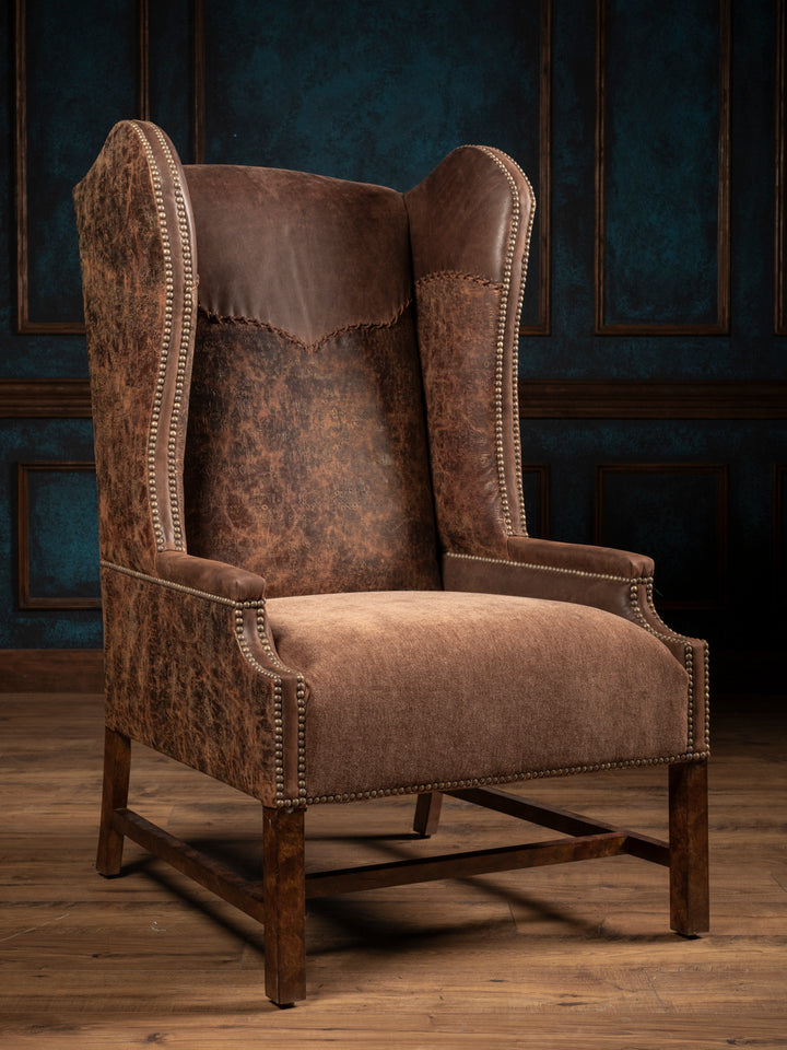 Stockman Western leather wingback chair with brown embossed leather, a velvet seat and yoke design in rustic room space.