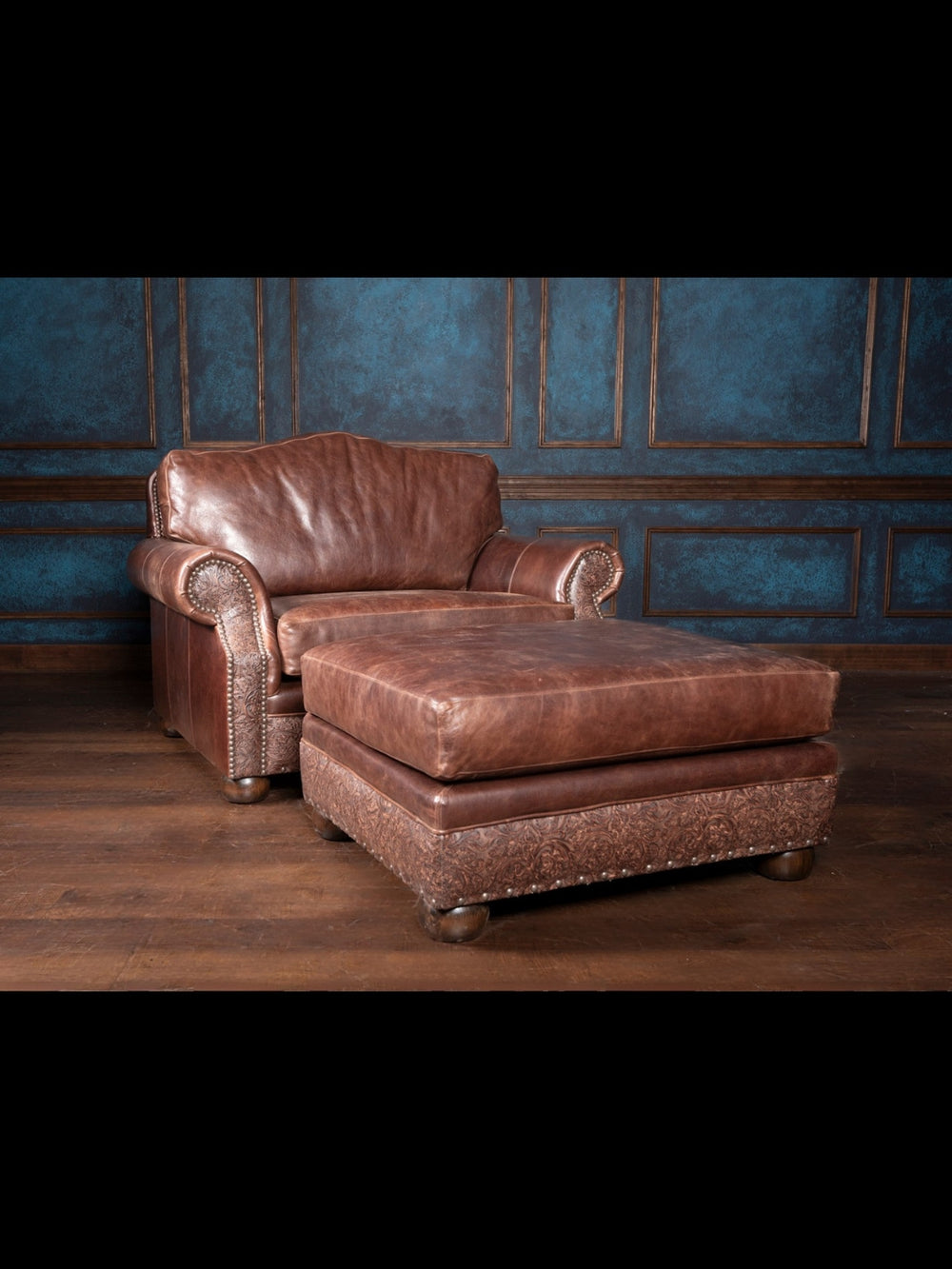 Texas leather chair and a half with ottoman in brown leather with a rolled arm design and intricate tooled leather panels in a western room.