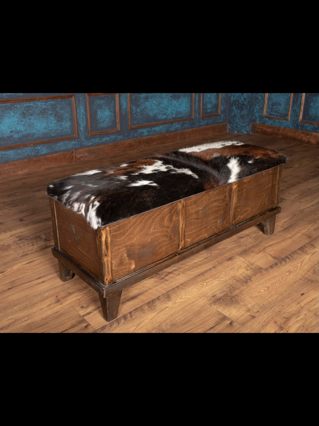Wooden bench with cowhide cover against a blue paneled wall.