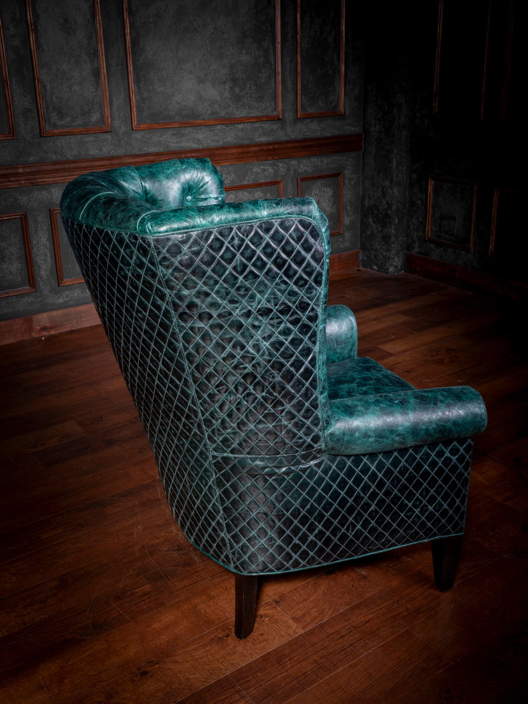 Tufted Teal Leather Wingback Chair with teal diamond-stitched quilted leather and straight black feet in a spacious rustic living room.
