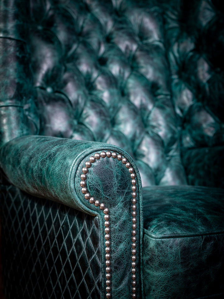 Tufted Teal Leather Wingback Chair in teal leather with diamond stitch accents featuring rolled arm design with silver nailheads in a close-up view.