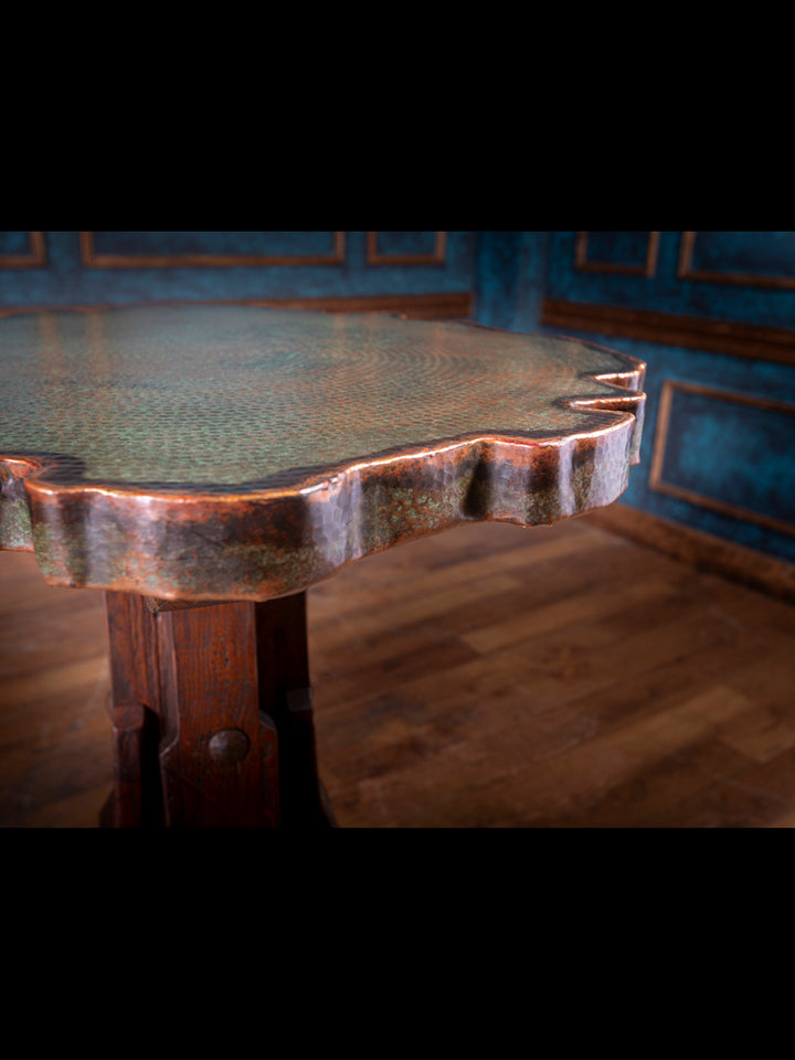 Detailed view of carved wood pedestal base with aged iron rivets supporting copper pub table.