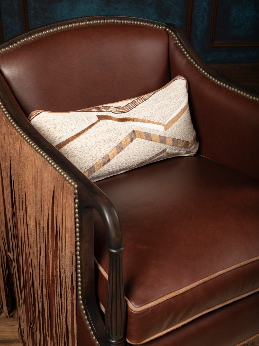 Macro interior detail of a custom western leather accent chair showcasing smooth warm cognac full-grain leather upholstery and a southwestern geometric fabric pillow.