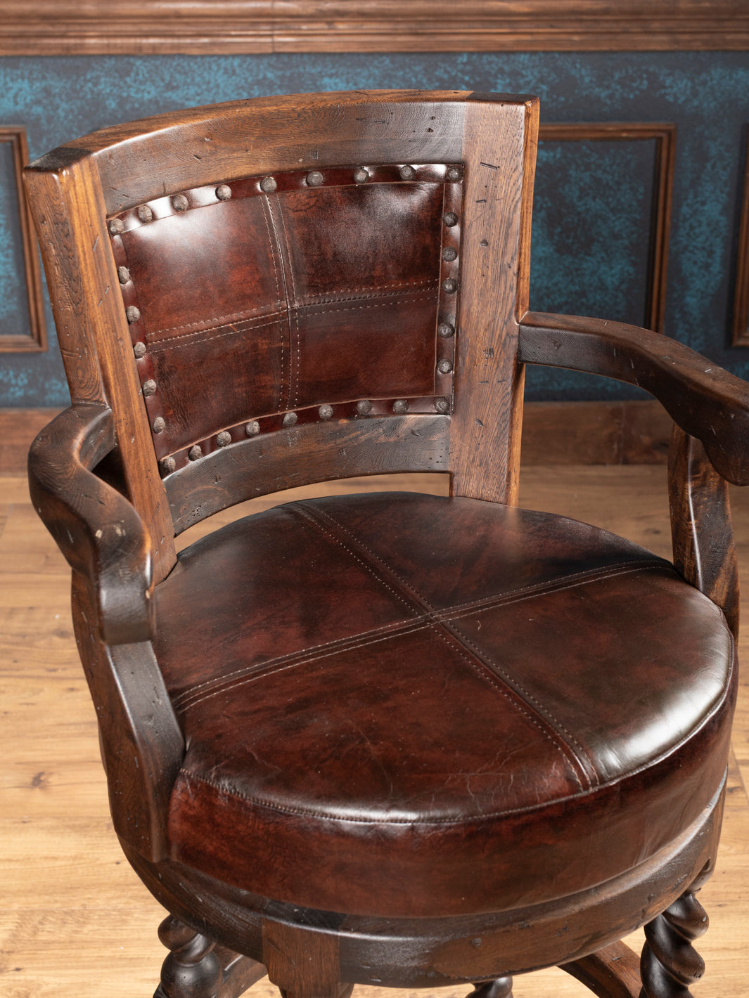Wooden bar stool with leather seat and backrest in a room with wooden floor and blue walls.