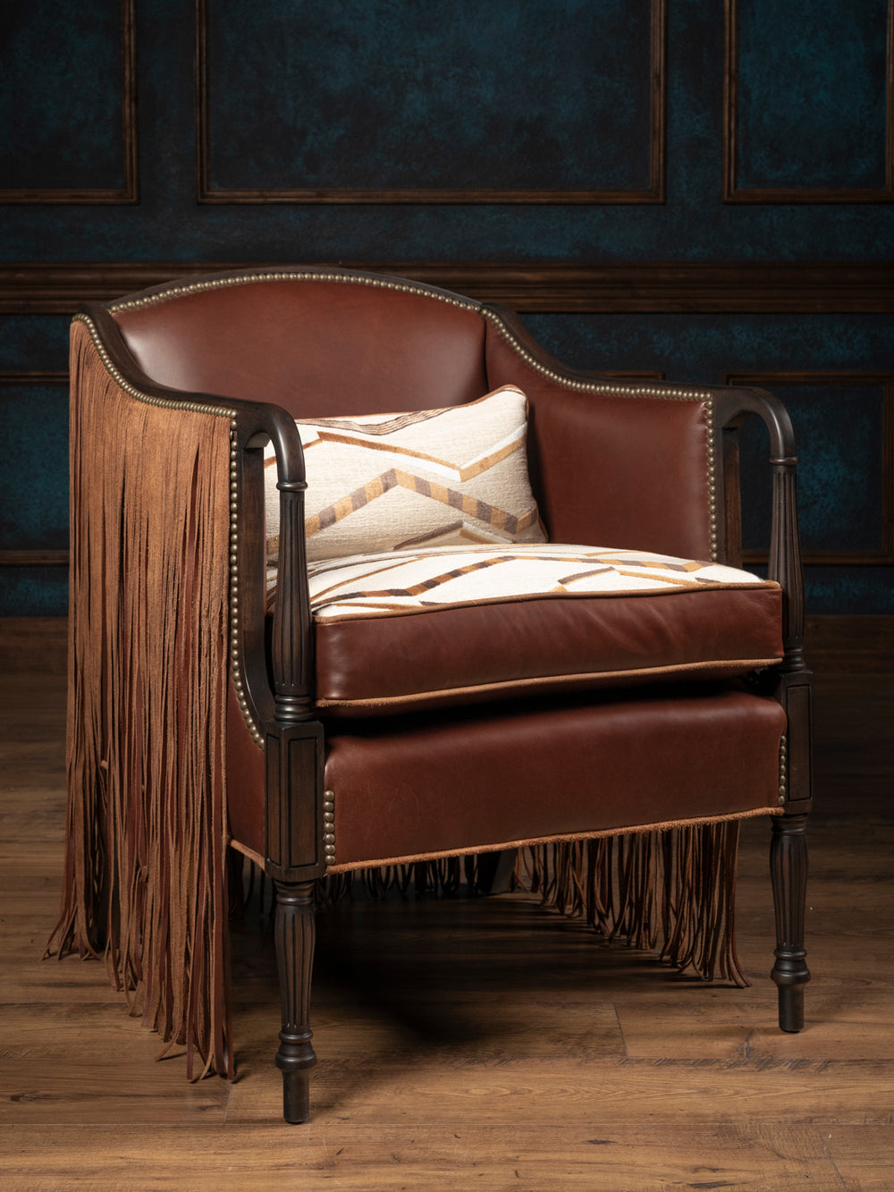 Low-angle straight view of the Boulder Western leather accent chair showcasing long hand-cut suede fringe panels and a patterned southwestern geometric cushion.