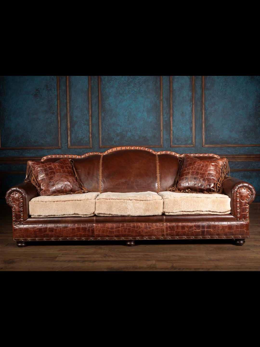 Front view of a ranch style leather and shearling sofa decorated with two matching crocodile-embossed fringed leather pillows.