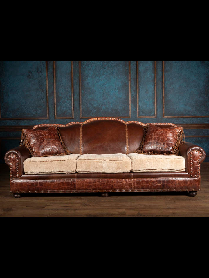 Front view of a ranch style leather and shearling sofa decorated with two matching crocodile-embossed fringed leather pillows.