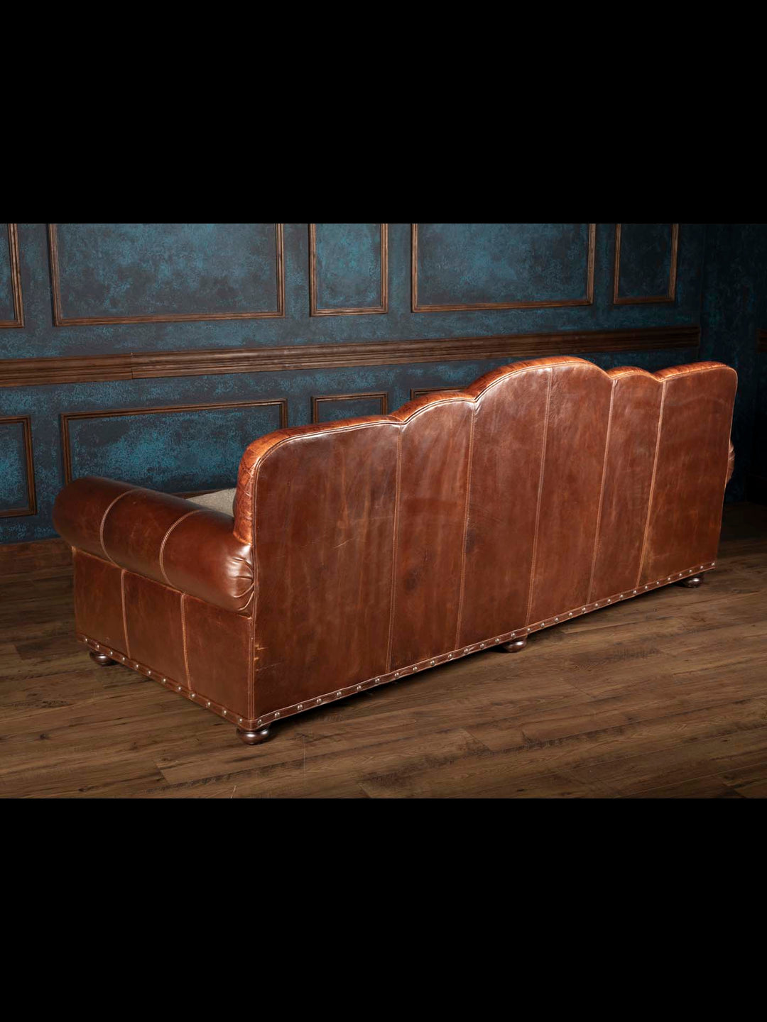 Rear view of a Western ranch style sofa showcasing panels of thick distressed brown full grain leather and bun feet.