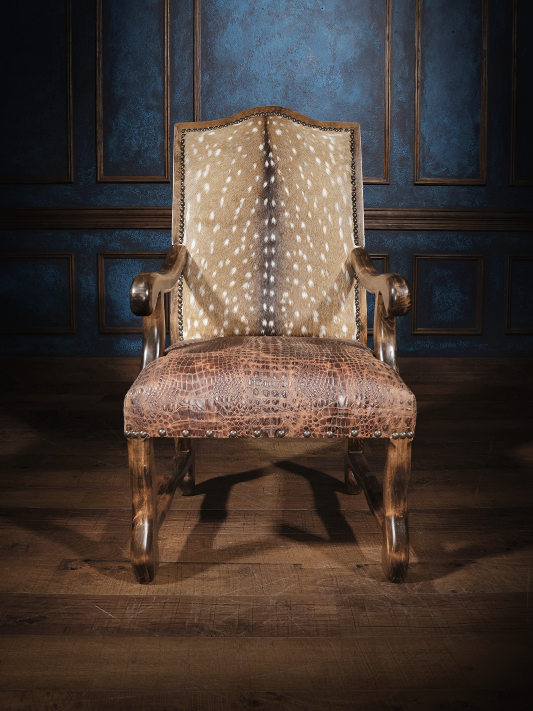 Front view of a wooden armchair featuring a backrest upholstered in embossed axis hide and a seat covered in crocodile-embossed leather, accented with nailhead trim.