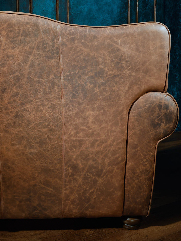 Close-up of the back panel of a western-style sectional sofa, showing distressed brown leather upholstery with smooth contours.