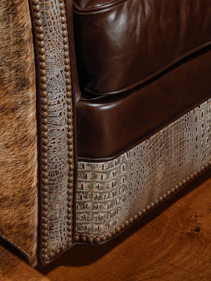 Close-up view of a western-style swivel chair showcasing a combination of hair-on-hide, brown leather, and crocodile-patterned leather, accented with nailhead trim.