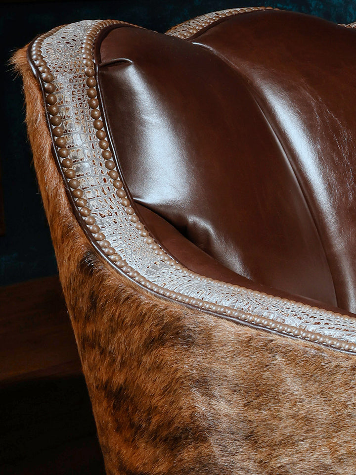 Close-up of a western-style swivel chair showing the combination of brown leather upholstery, hair-on-hide exterior, and crocodile-patterned leather trim with nailhead detailing.