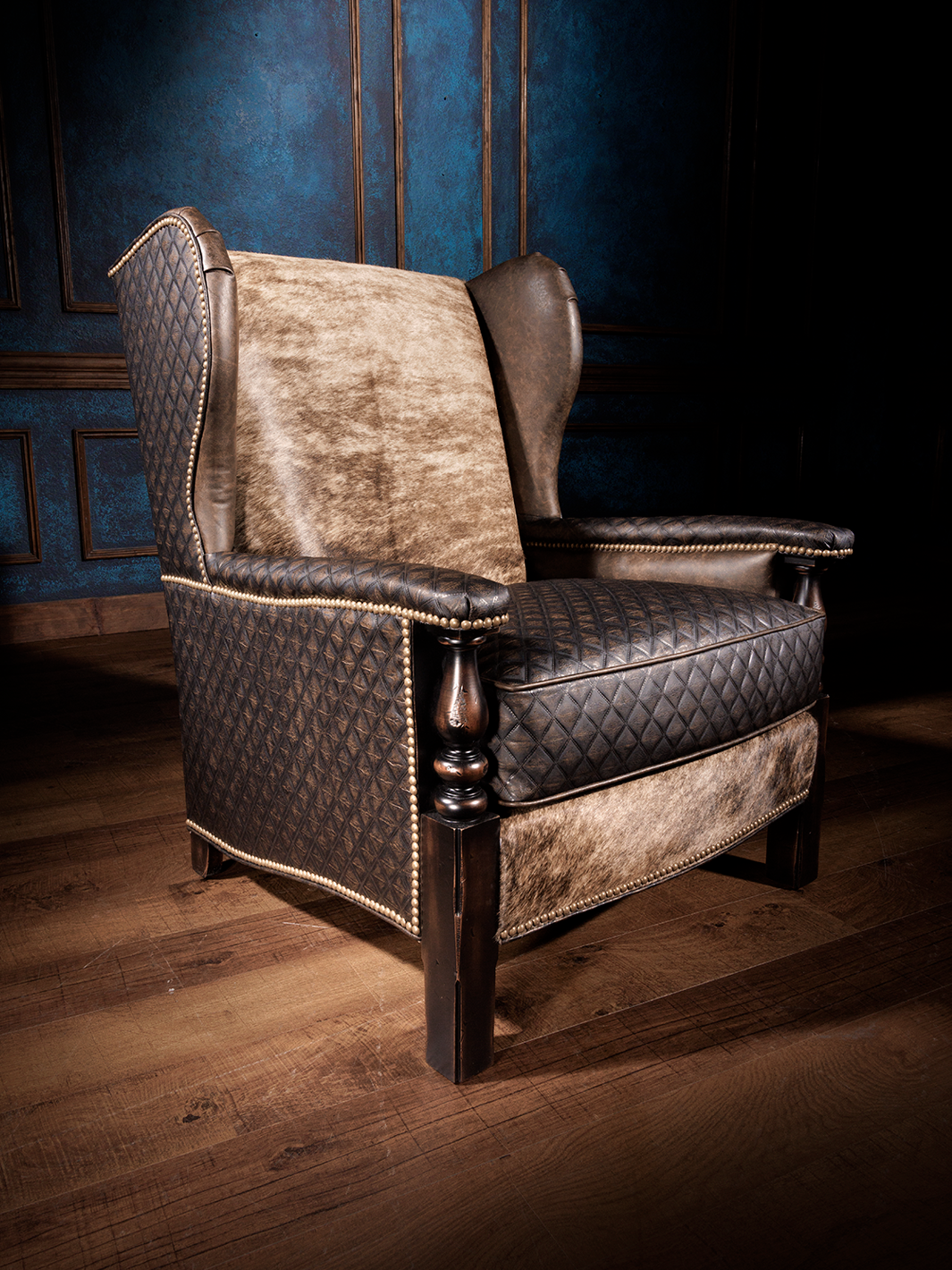 A wingback accent chair featuring quilted leather upholstery on the arms and sides, with brindle hair-on-hide accents on the backrest and seat, complemented by nailhead trim.