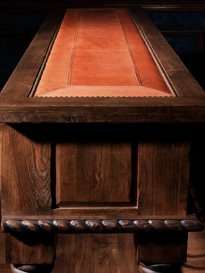 Close-up of a wooden table with a brown leather inlay, featuring detailed craftsmanship and a rustic finish.