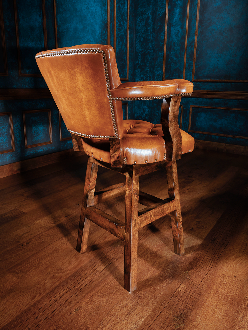 back view of wooden barstool with a button-tufted leather seat and backrest, featuring armrests and nailhead trim, upholstered in rich tan leather