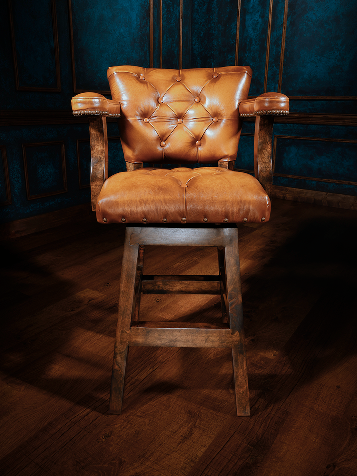 front view of wooden barstool with a button-tufted leather seat and backrest, featuring armrests and nailhead trim, upholstered in rich tan leather