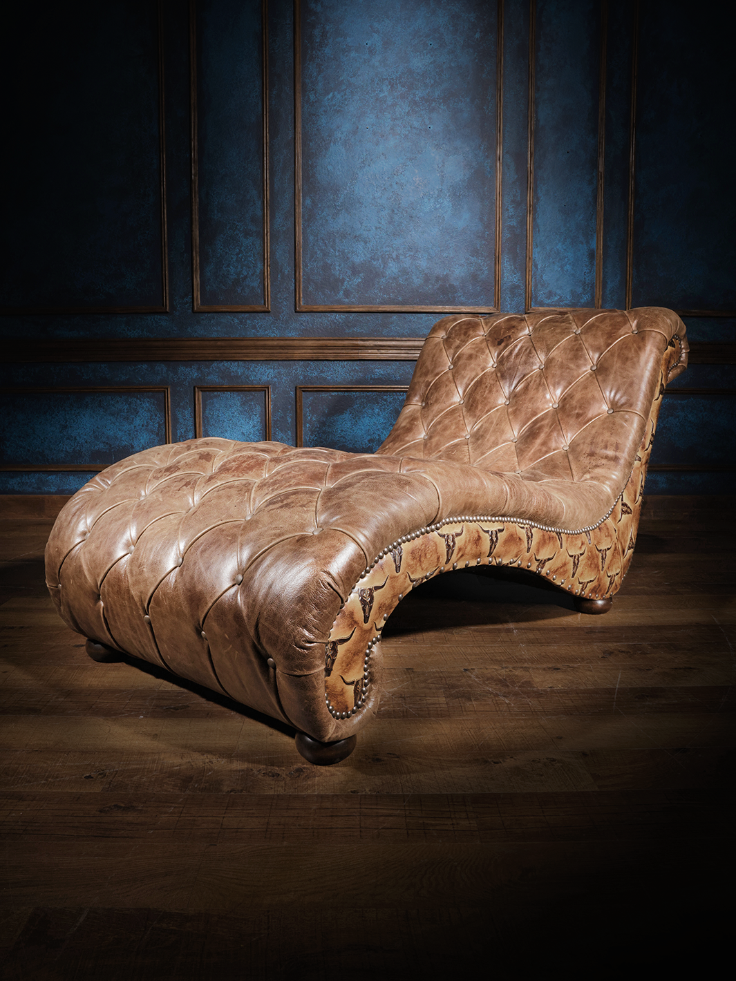 A luxurious chaise lounge upholstered in tufted brown leather with intricate nailhead trim, featuring embossed leather accents on the sides, adding a western flair.