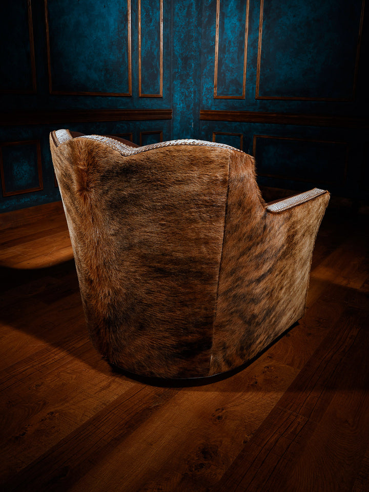 Back view of a western-style swivel chair fully upholstered in hair-on-hide, with crocodile-patterned leather trim and nailhead detailing along the edges.